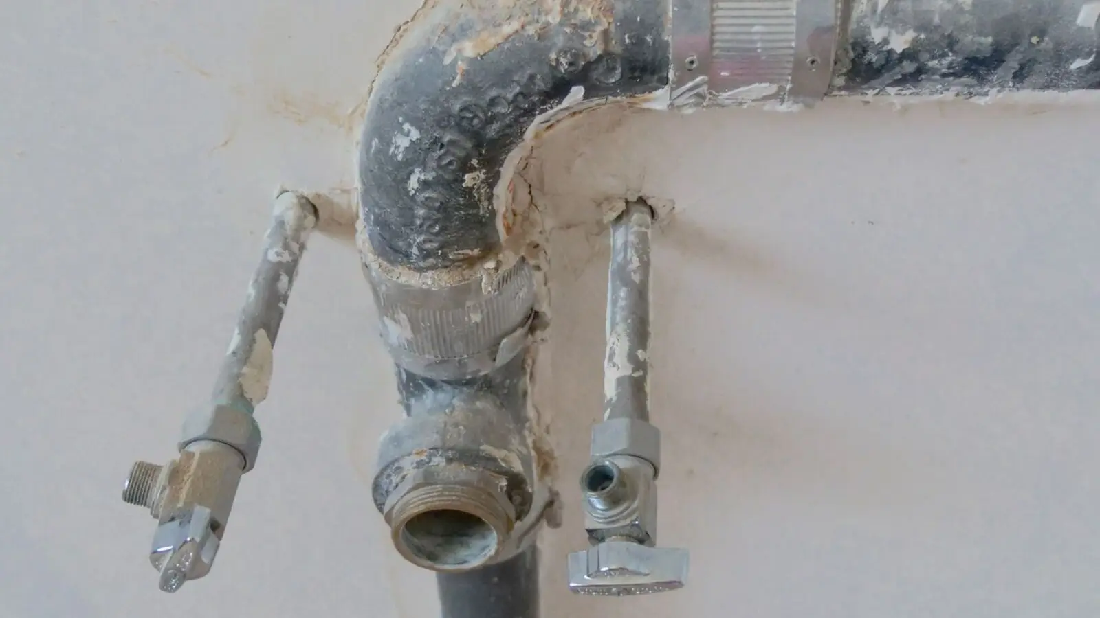 Corroded galvanized pipework and old shut-off valves on a utility wall